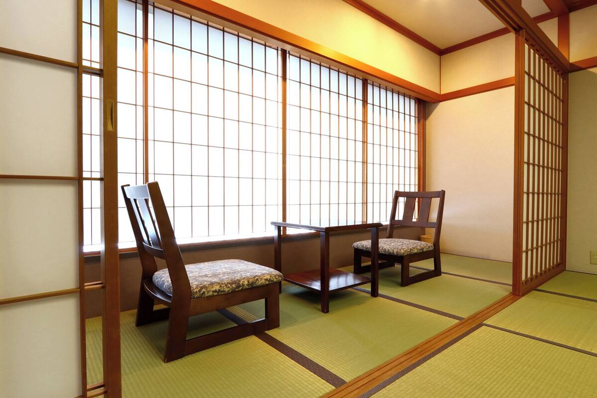 Ein traditioneller japanischer Raum mit Tatami-Böden, Shoji-Schirmen und zwei Holzstühlen.