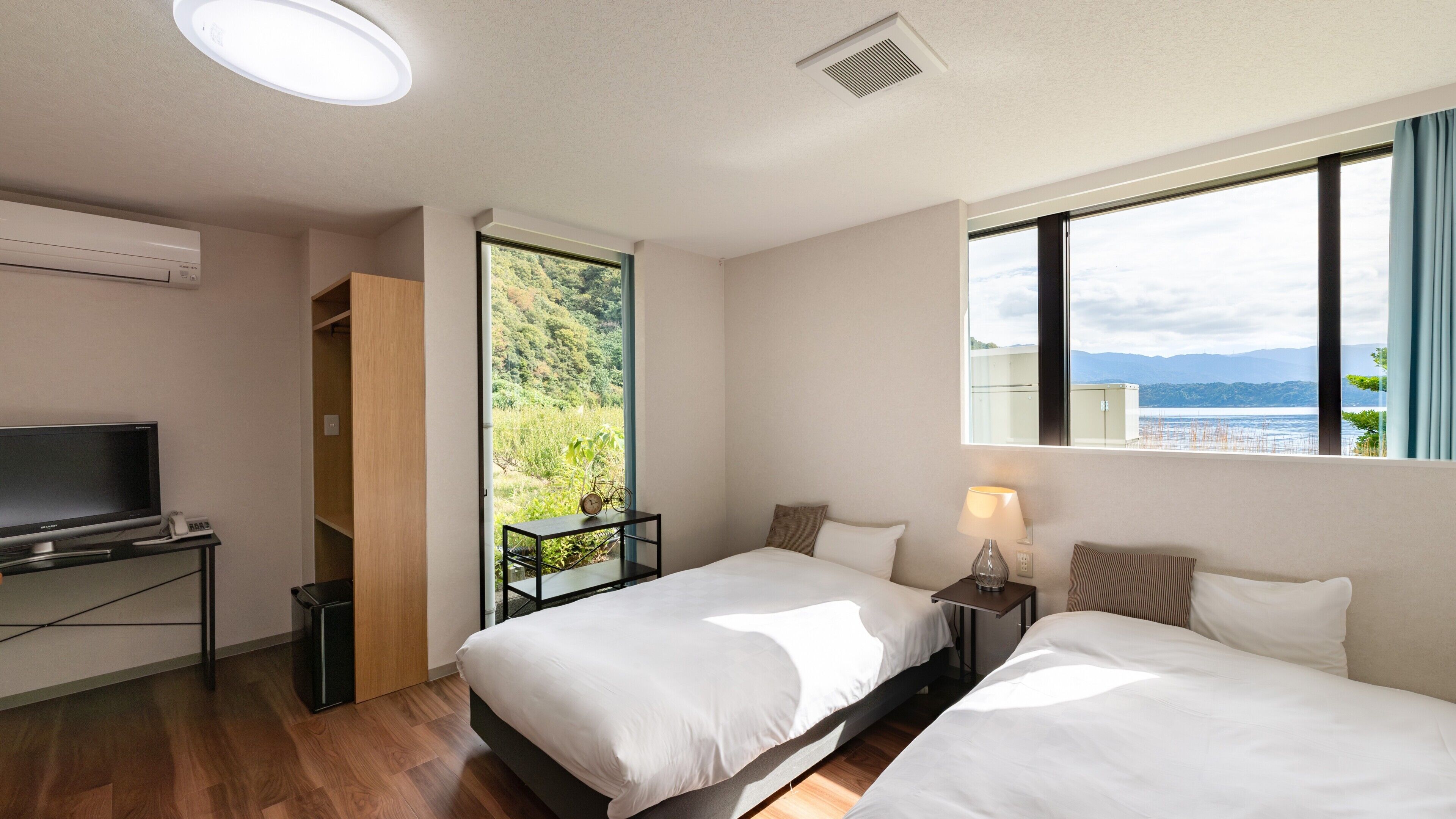 A hotel room with two beds, a TV, a desk, and a window with a view of a mountainous landscape.