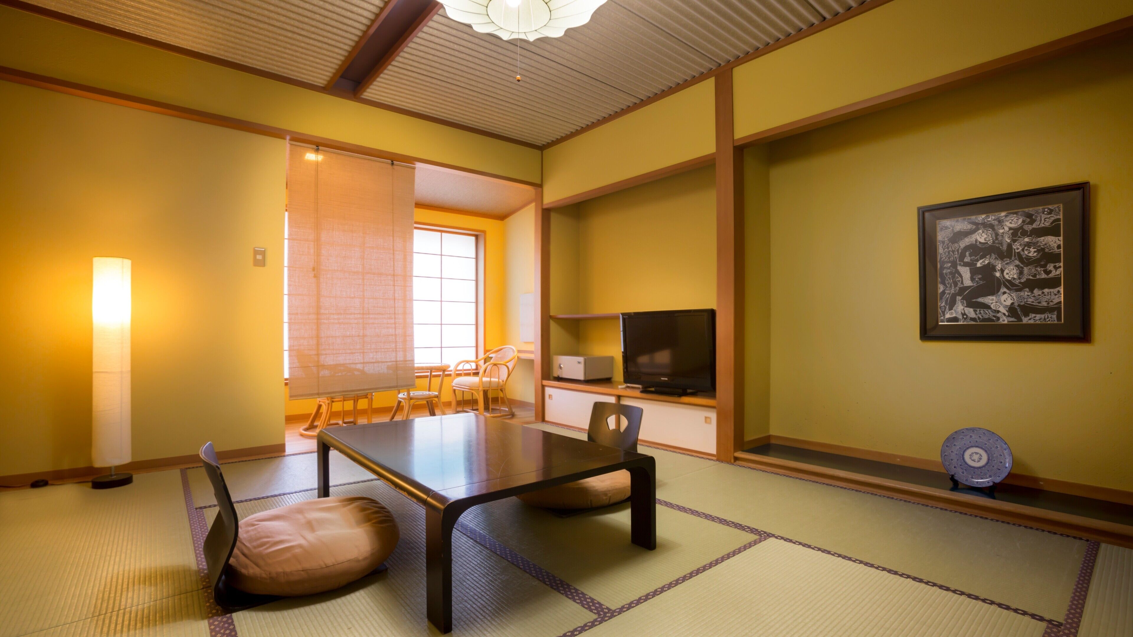 A traditional Japanese room with tatami flooring, a low table, chairs, a television, and a framed picture on the wall.