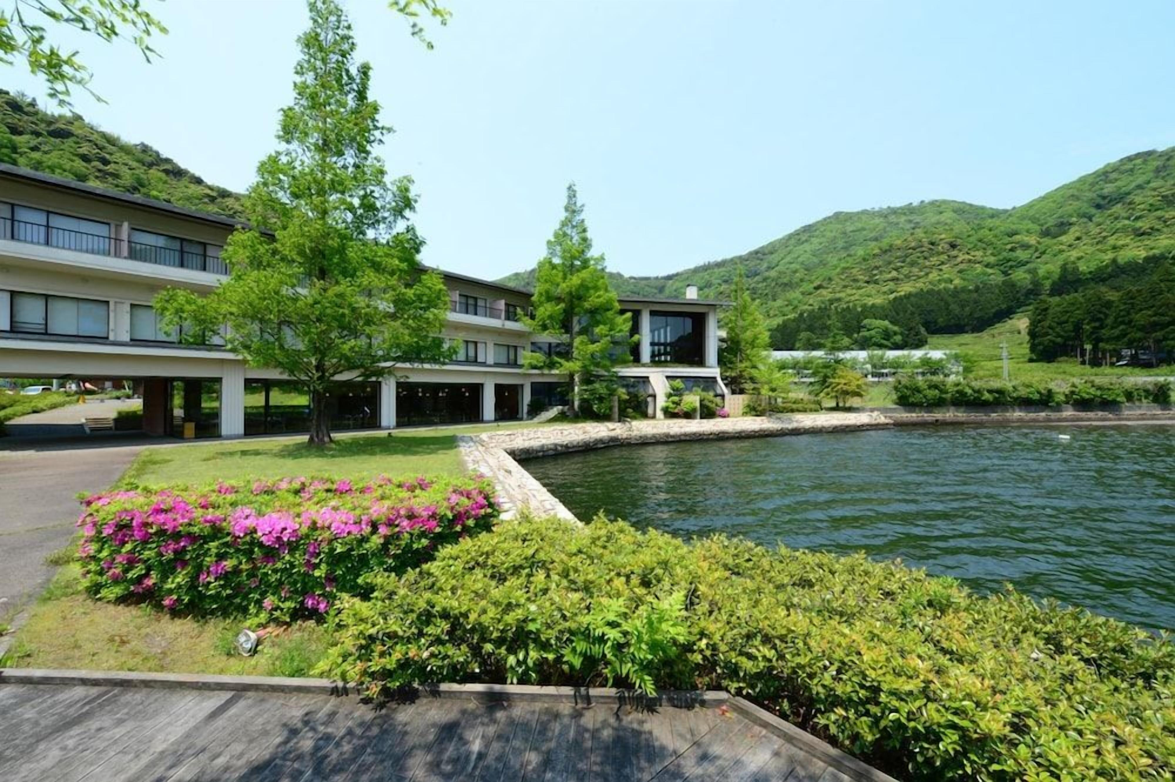 A modern building with a swimming pool, surrounded by lush greenery and hills.
