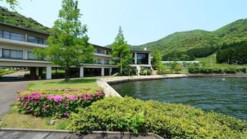 A modern building with a swimming pool, surrounded by lush greenery and hills.
