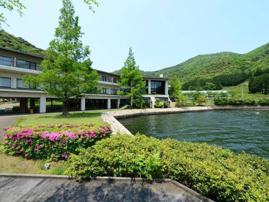 A modern building with a swimming pool, surrounded by lush greenery and hills.