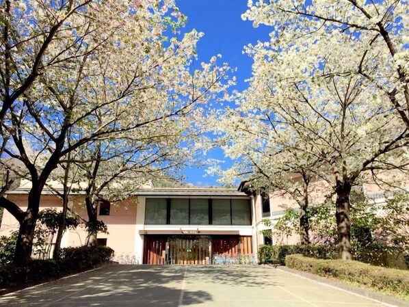 A building with a large glass facade, surrounded by trees with white blossoms, and a clear blue sky. - Wakasamikata Kirara Onsen Hotel Suigekka (Wakasa)