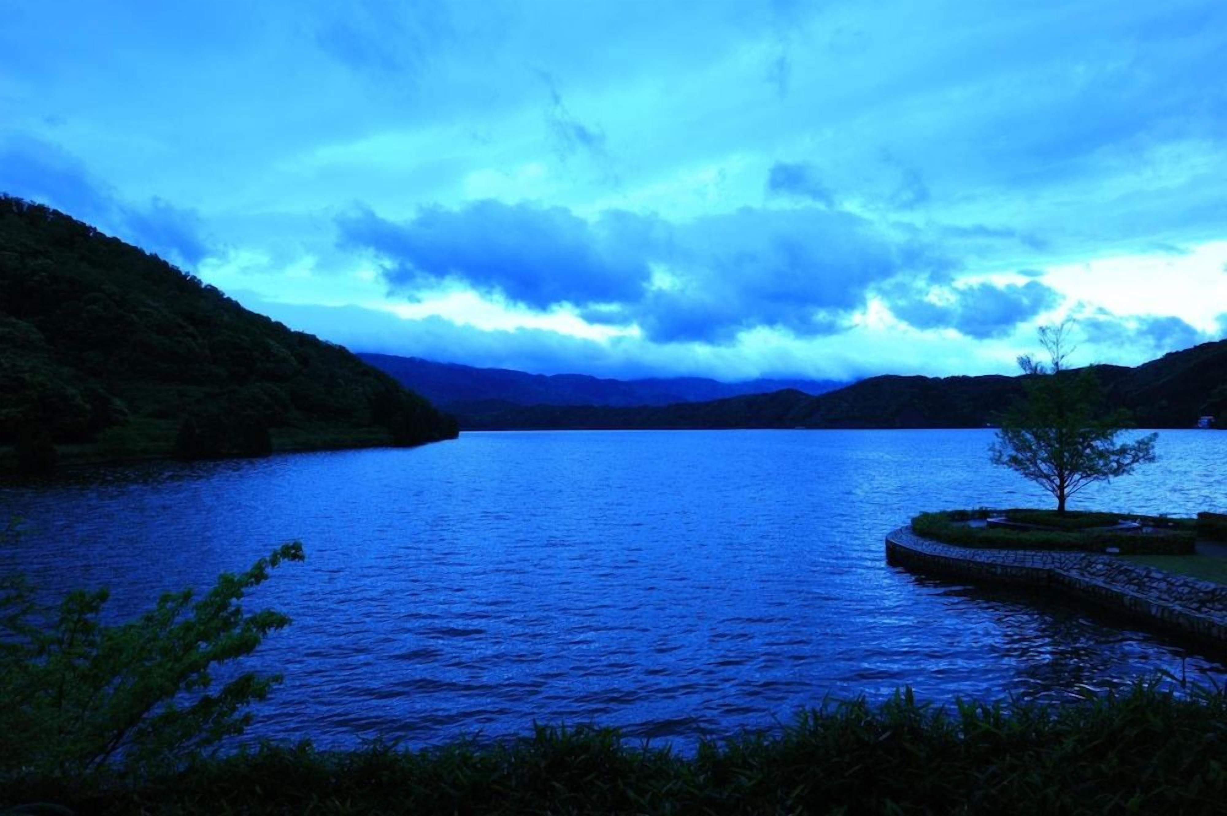 A serene lake surrounded by hills, with a clear sky above.