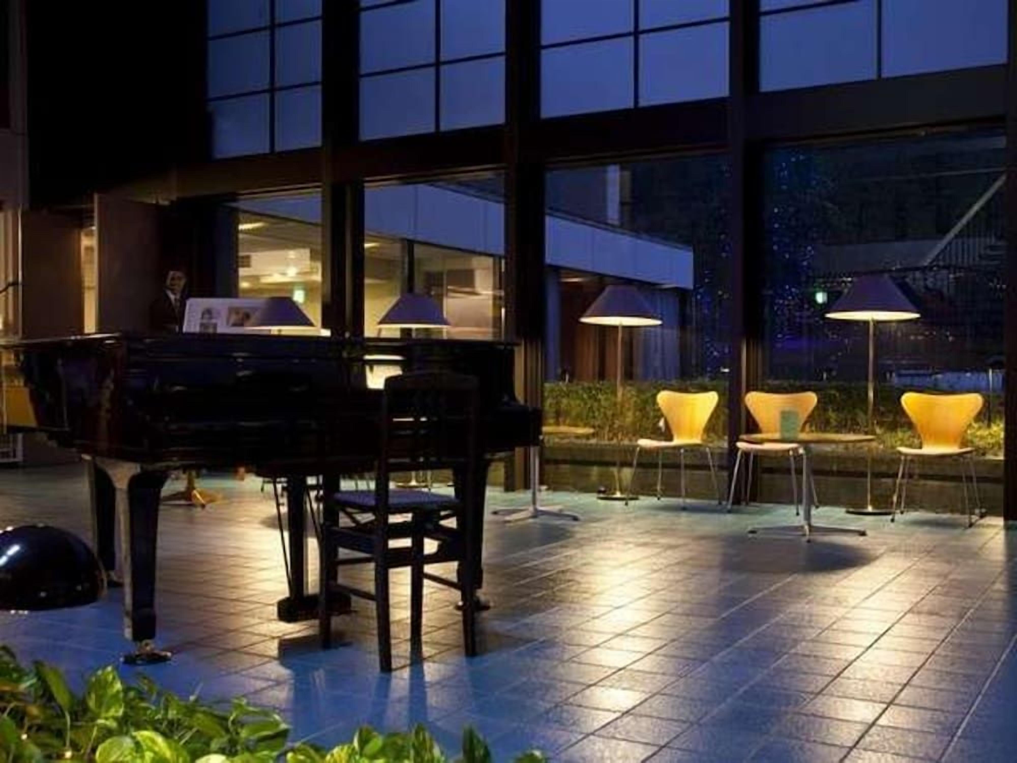 A piano in an outdoor area with chairs and tables, large windows, and a view of the city.