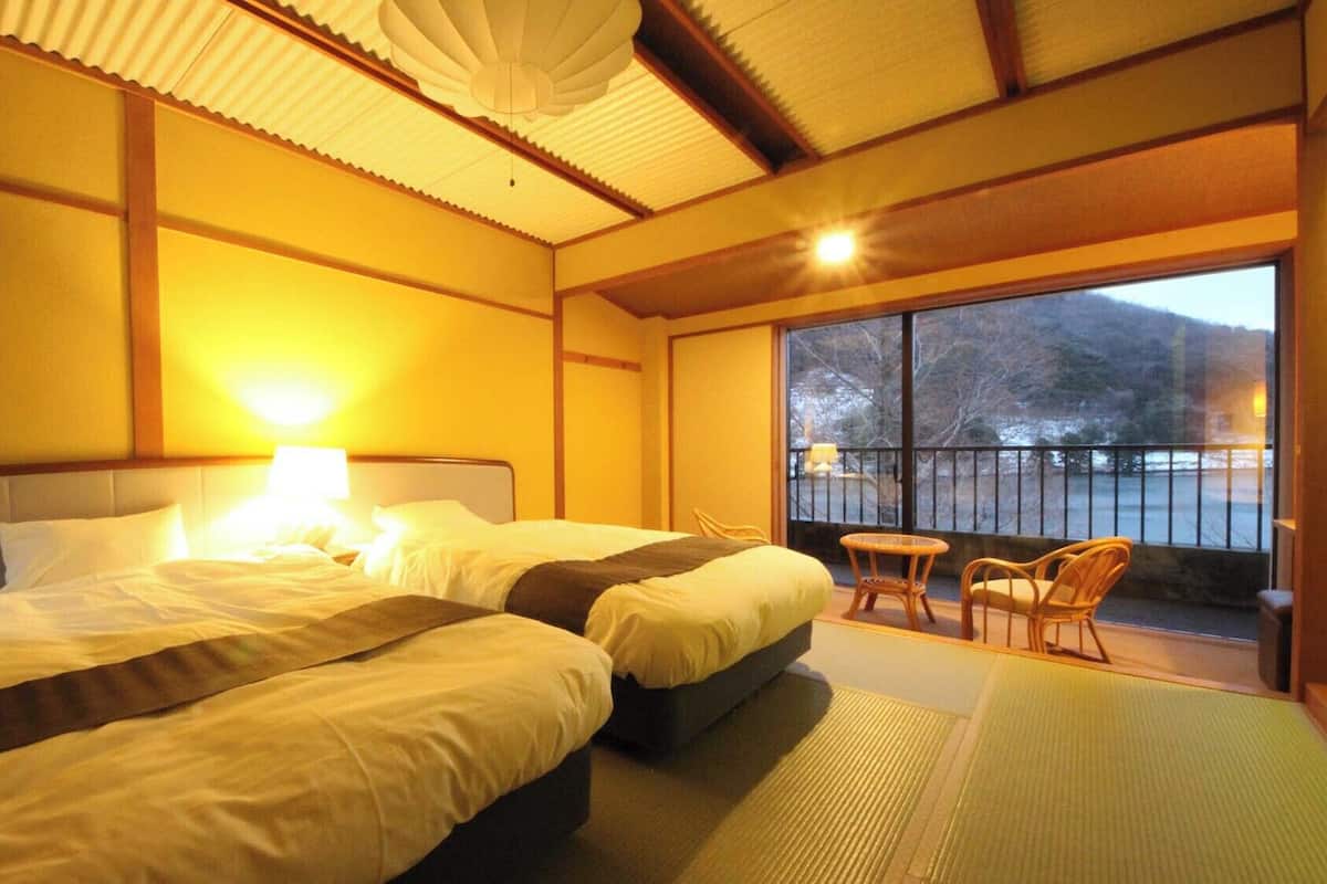 Habitación de hotel con dos camas, un balcón con sillas y un ventanal grande.