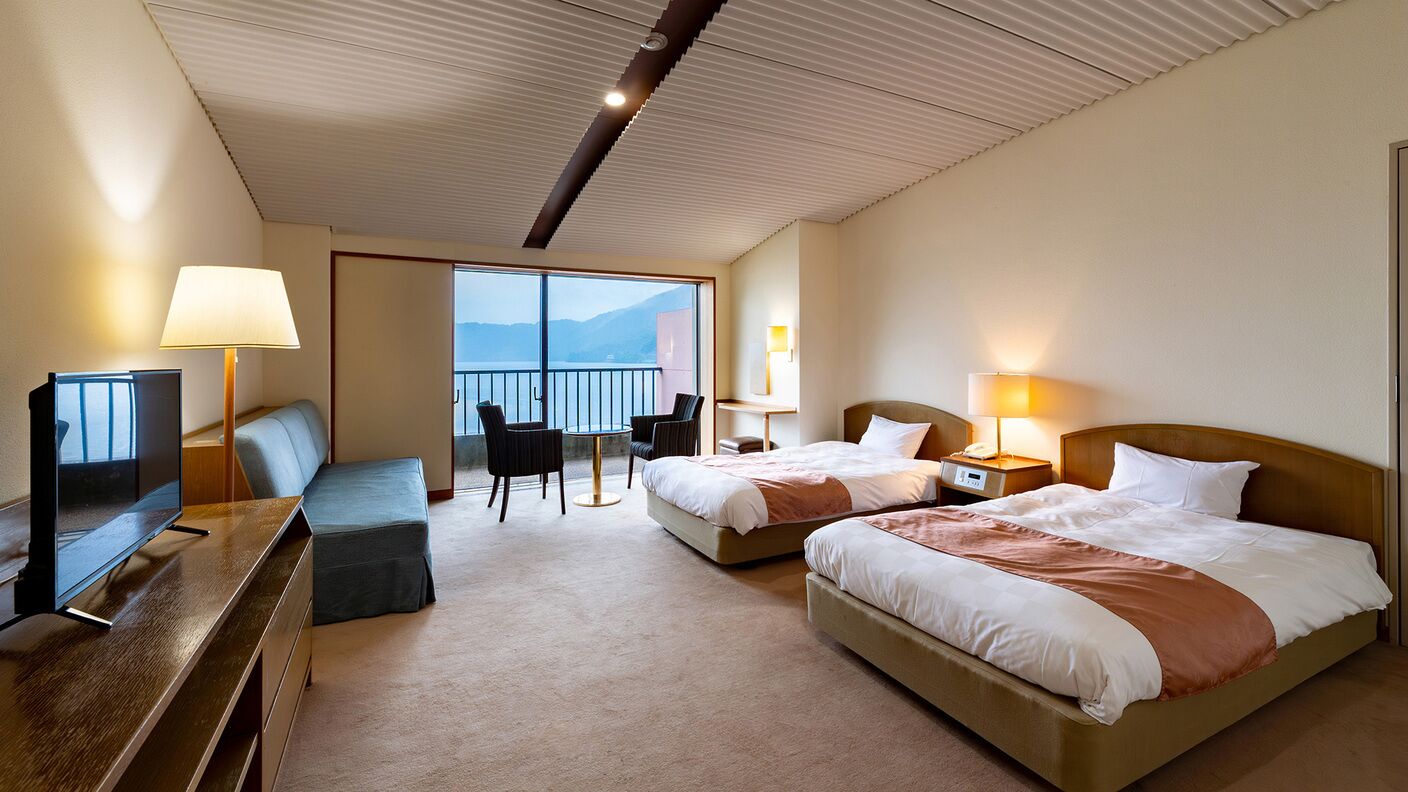 Ein Hotelzimmer mit zwei Betten, einem Fernseher, einem Schreibtisch und einem Balkon mit Blick.