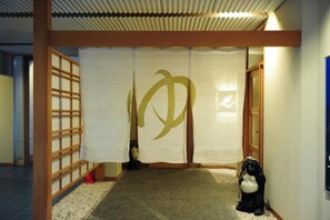 A traditional Japanese interior with tatami flooring, a shoji screen with a golden symbol, and a black and white statue. - Wakasamikata Kirara Onsen Hotel Suigekka (Wakasa)