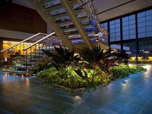 A spacious indoor area with a prominent staircase, a seating area with tables, and a large window providing a view of the outside. - Wakasamikata Kirara Onsen Hotel Suigekka (Wakasa)