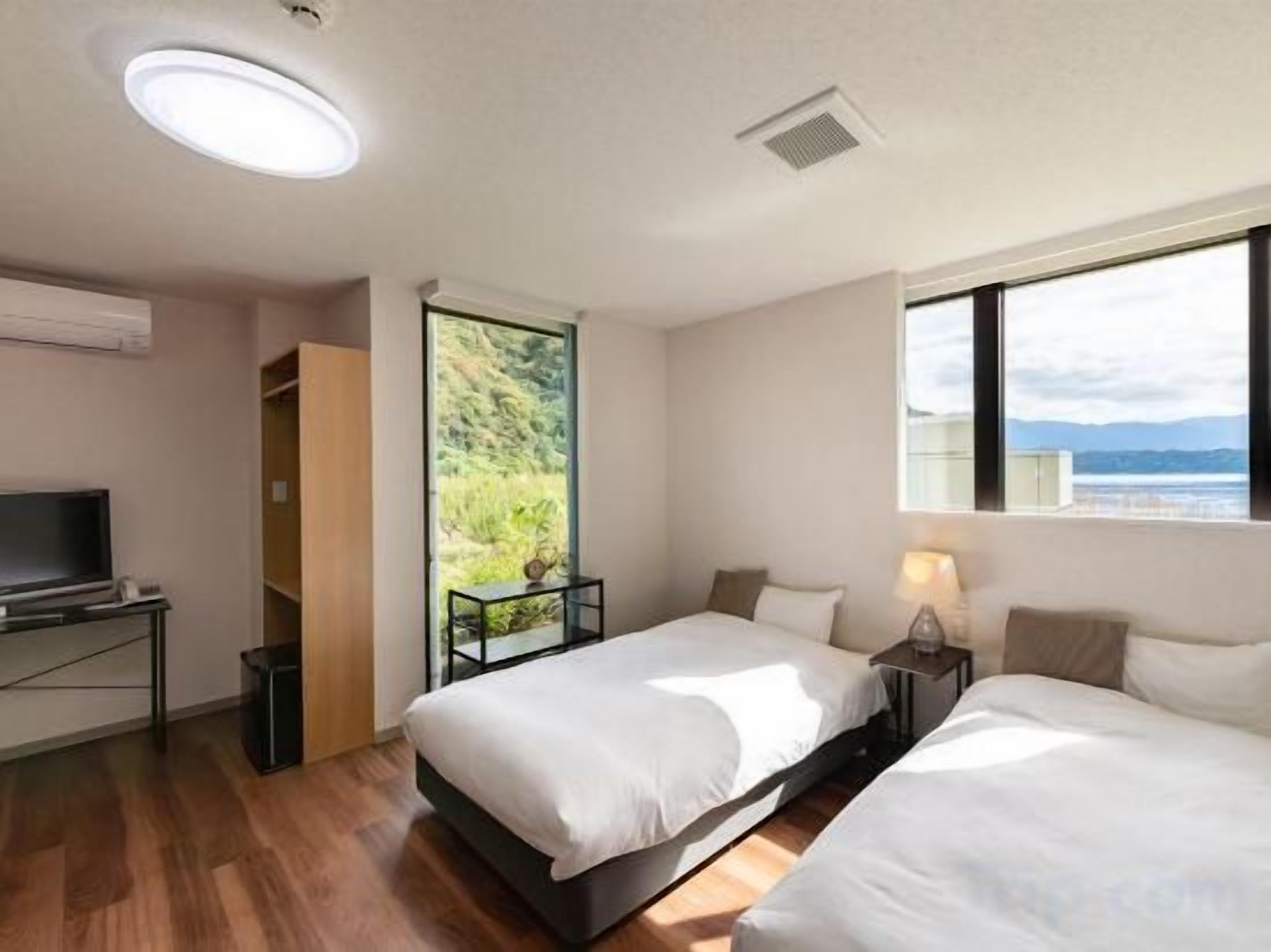 Quarto de hotel com duas camas, uma secretária com televisão, janela com vista para o mar e porta que dá para uma varanda.