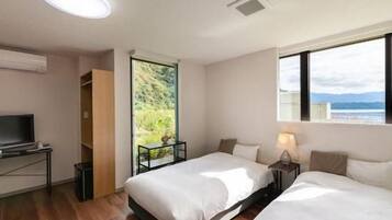 Quarto de hotel com duas camas, uma secretária com televisão, janela com vista para o mar e porta que dá para uma varanda.