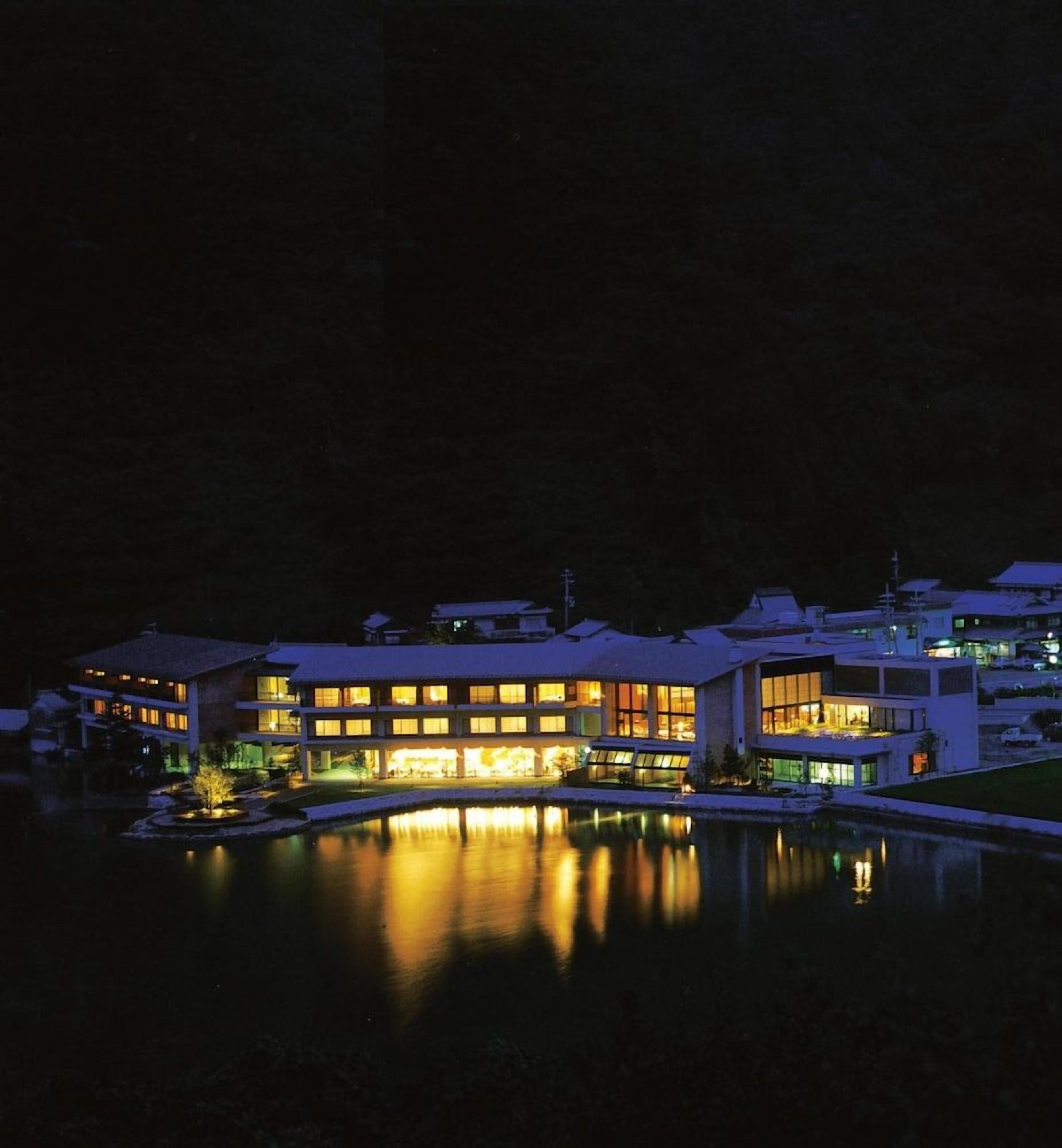 A multi-story hotel with illuminated windows and a reflection in the water.