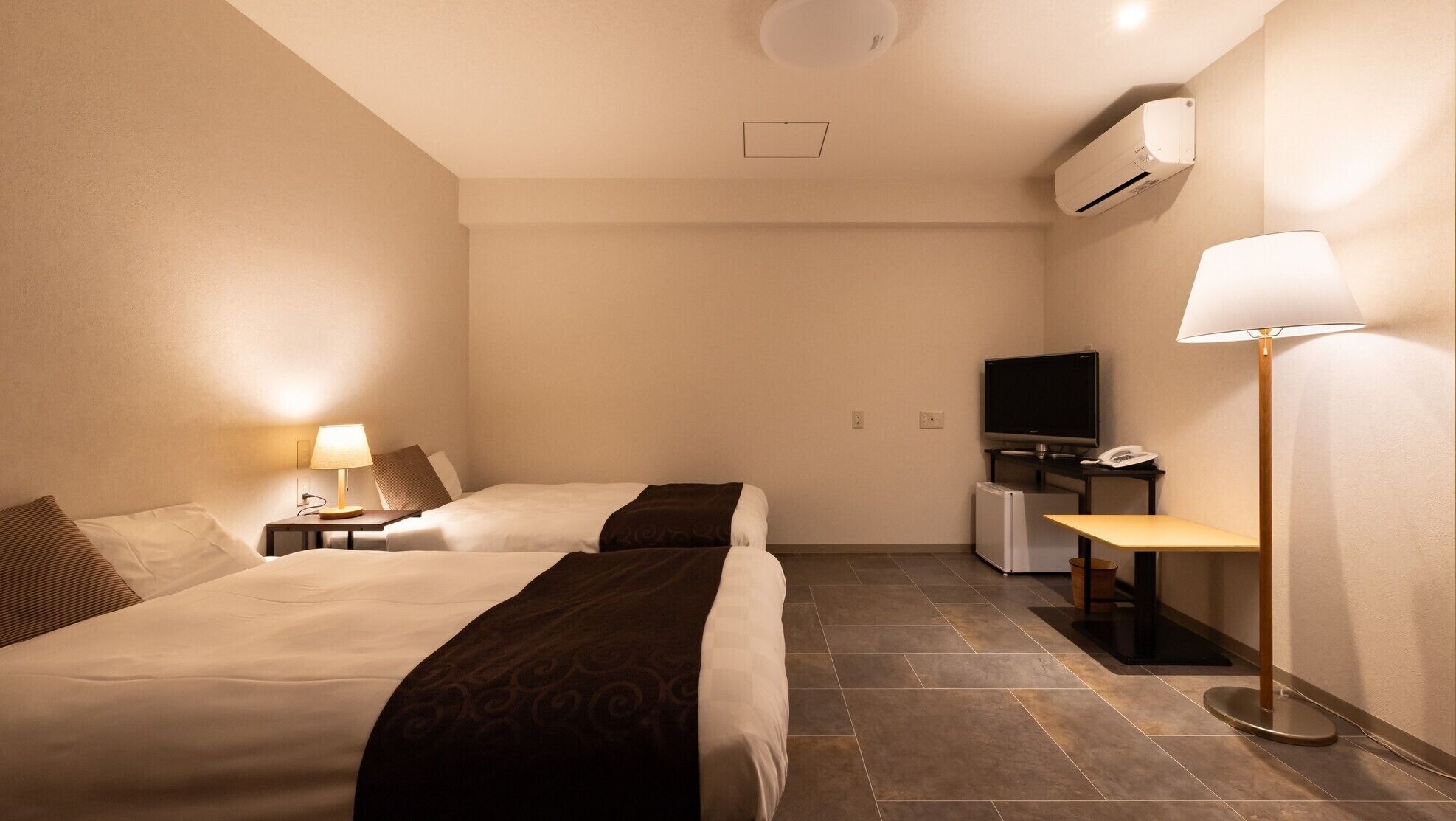 Ein Hotelzimmer mit zwei Betten, einem Schreibtisch, einem Computer, einem Fernseher und einer Lampe.