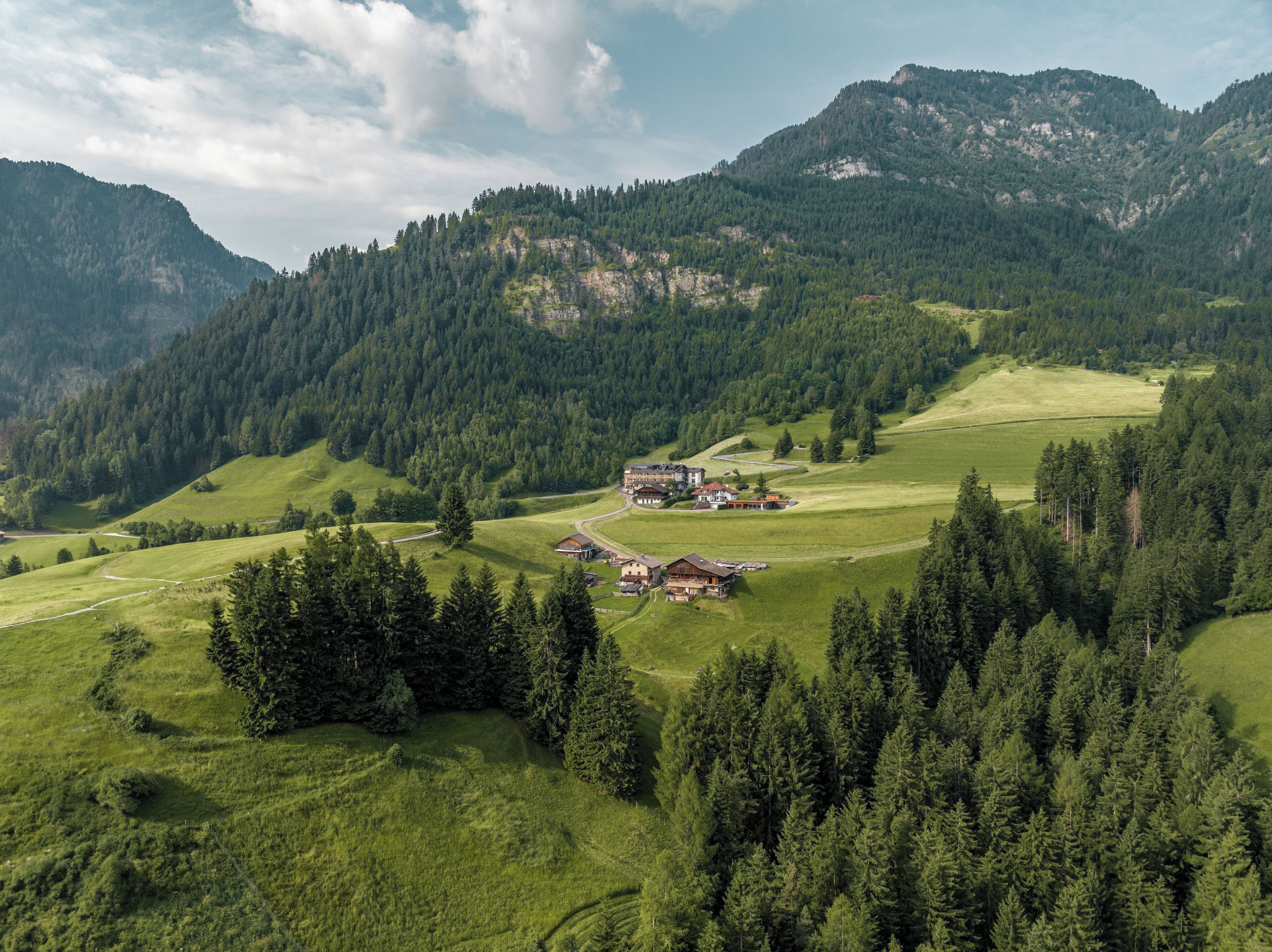 A rural landscape with a cluster of buildings surrounded by dense forests and rolling hills.