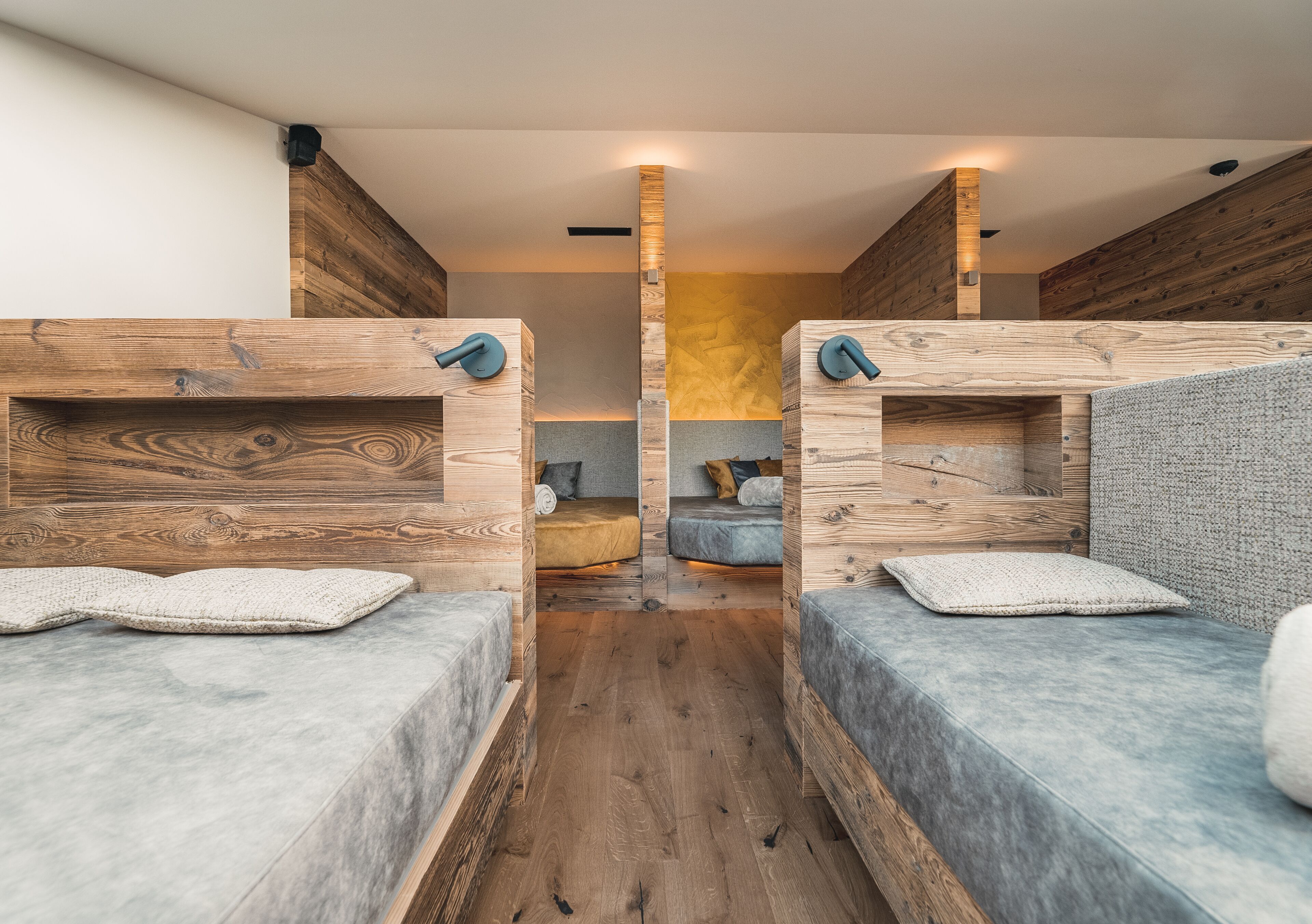 A modern, compact room with two wooden bunk beds, a central light fixture, and a small seating area with cushions.