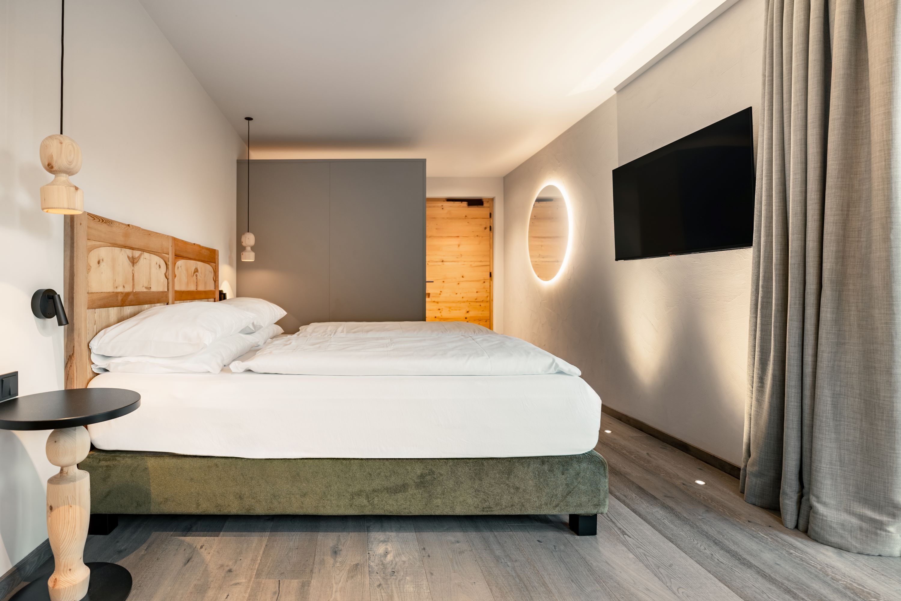A modern bedroom with a bed, a round mirror, a flat-screen TV, and a wooden headboard.