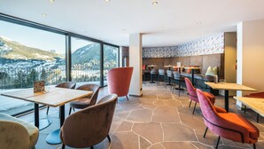 A modern dining area with large windows, stone flooring, and contemporary furniture.