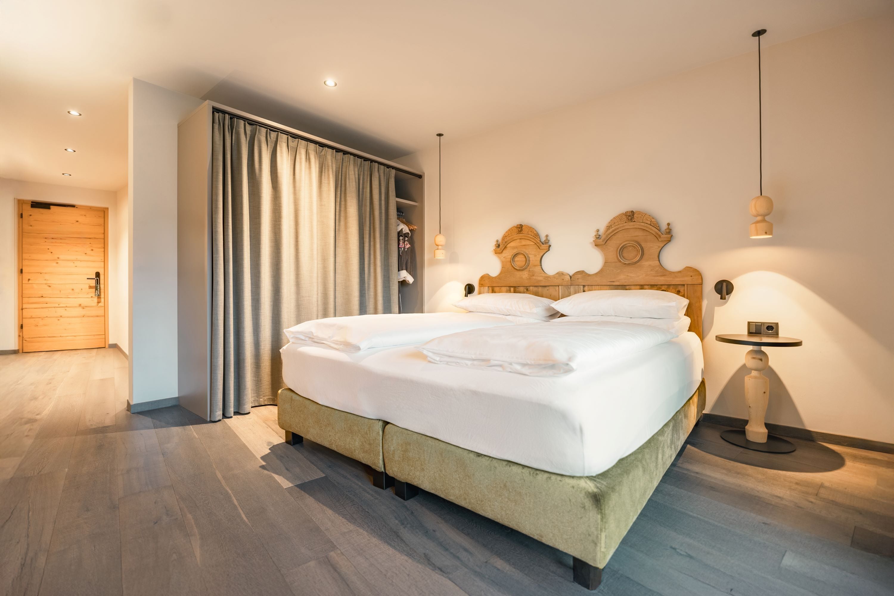 Una habitación de hotel moderna con una cama de madera, una mesita de noche pequeña y un armario con cortina.