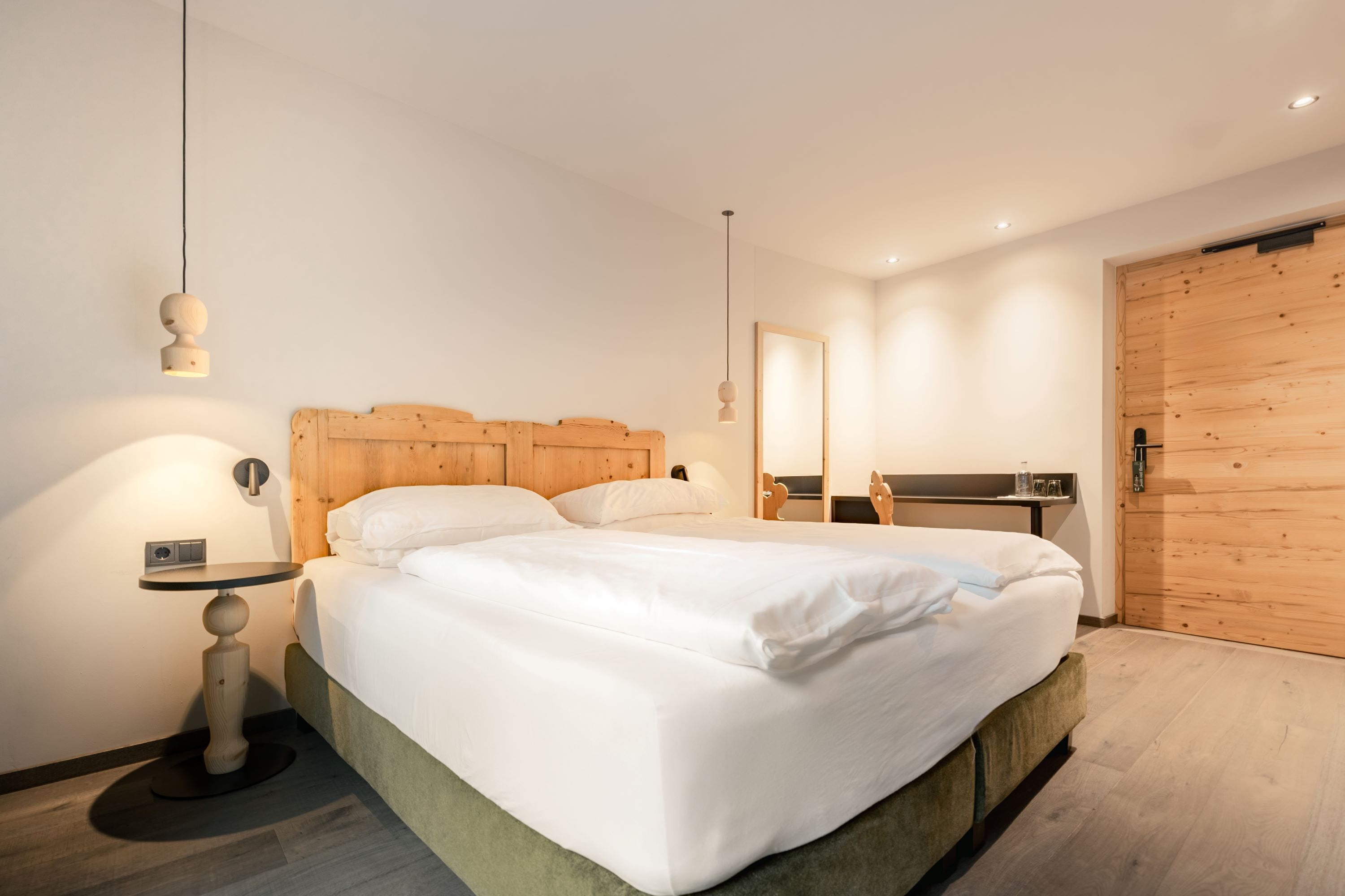 Un dormitorio moderno con cabecera de madera, una mesita de noche redonda y una cama grande con ropa blanca de cama.