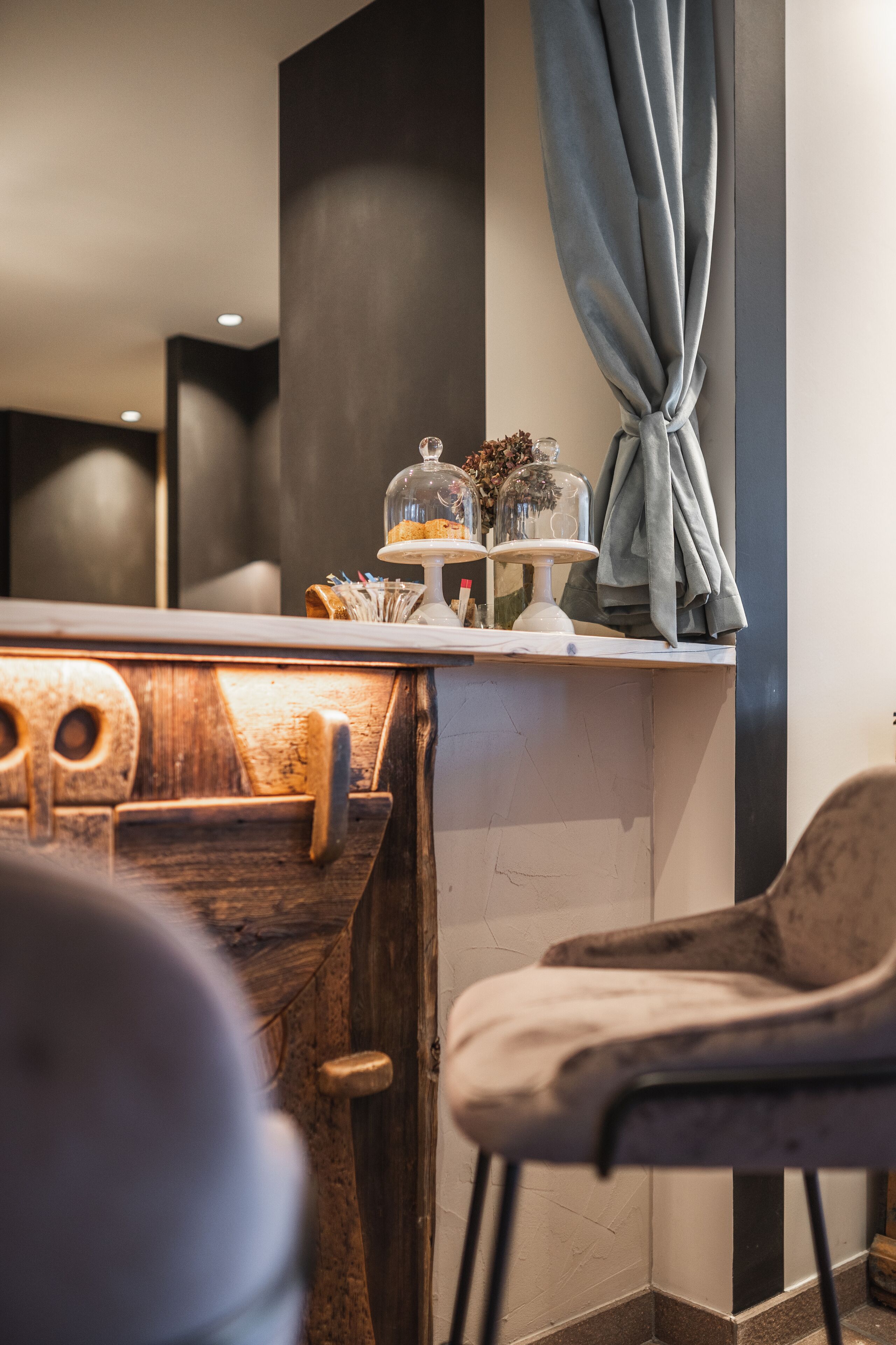 A modern interior with a wooden counter, a grey chair, and a decorative glass dome on the shelf.