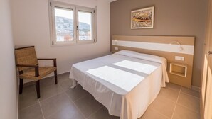 A bedroom with a bed, a chair, a window, and a painting on the wall.