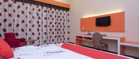 Una habitación de hotel con cama, escritorio, silla, televisor y un sillón rojo.