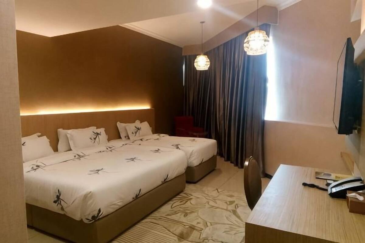 A hotel room with two beds, a desk, a chair, a TV, and a large window with curtains.