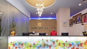 A hotel reception desk with a modern design, including a wooden reception desk, a chandelier, and framed pictures on the wall. - Hotel Holmes GP (Gelang Patah)