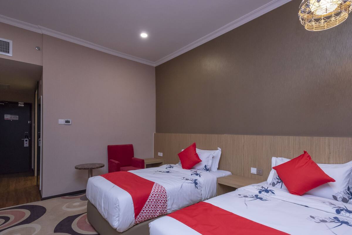 A hotel room with two beds, each with red and white bedding, a small red chair, a round table, and a modern light fixture.