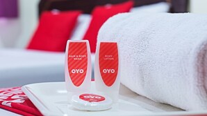 A hotel room with a neatly made bed, a white bath mat, and two bottles of OYO body wash and lotion on a tray. - Hotel Holmes GP (Gelang Patah)
