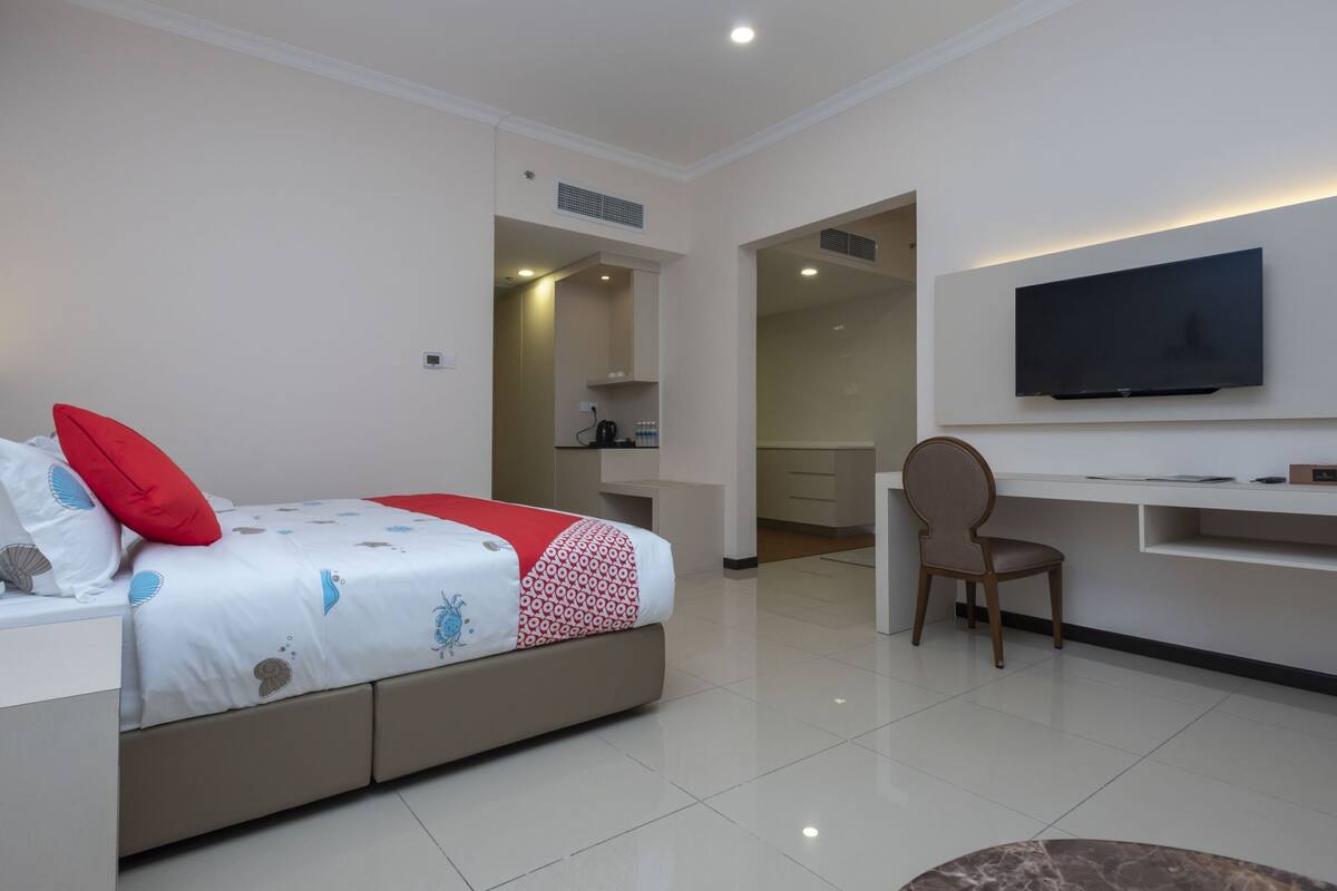 A modern hotel room with a bed, a desk, a chair, a television, and a bathroom visible through an open door.