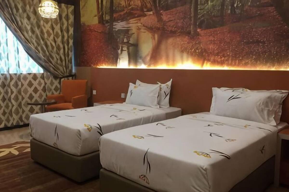 A hotel room with two beds, a large mural, a patterned curtain, and a modern chair.