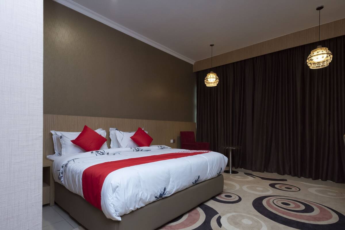 A hotel room with a large bed, red and white bedding, a patterned carpet, and two pendant lights.