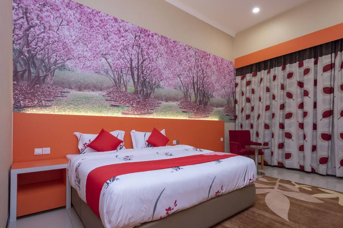 A modern bedroom with a large bed, orange accent walls, and a mural of cherry blossoms.