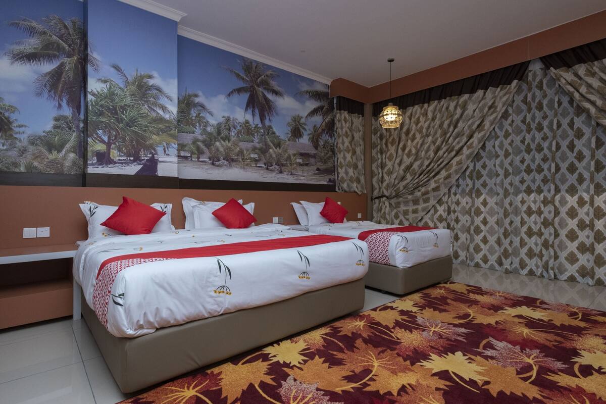 A hotel room with two beds, a large tropical mural, patterned curtains, and a decorative rug.