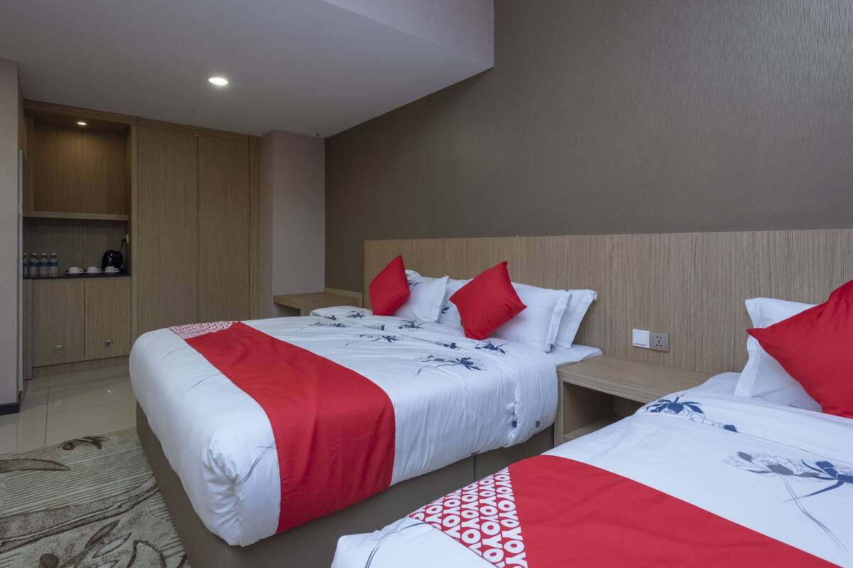 A hotel room with two beds, each with red and white bedding, a wooden headboard, and a bedside table.