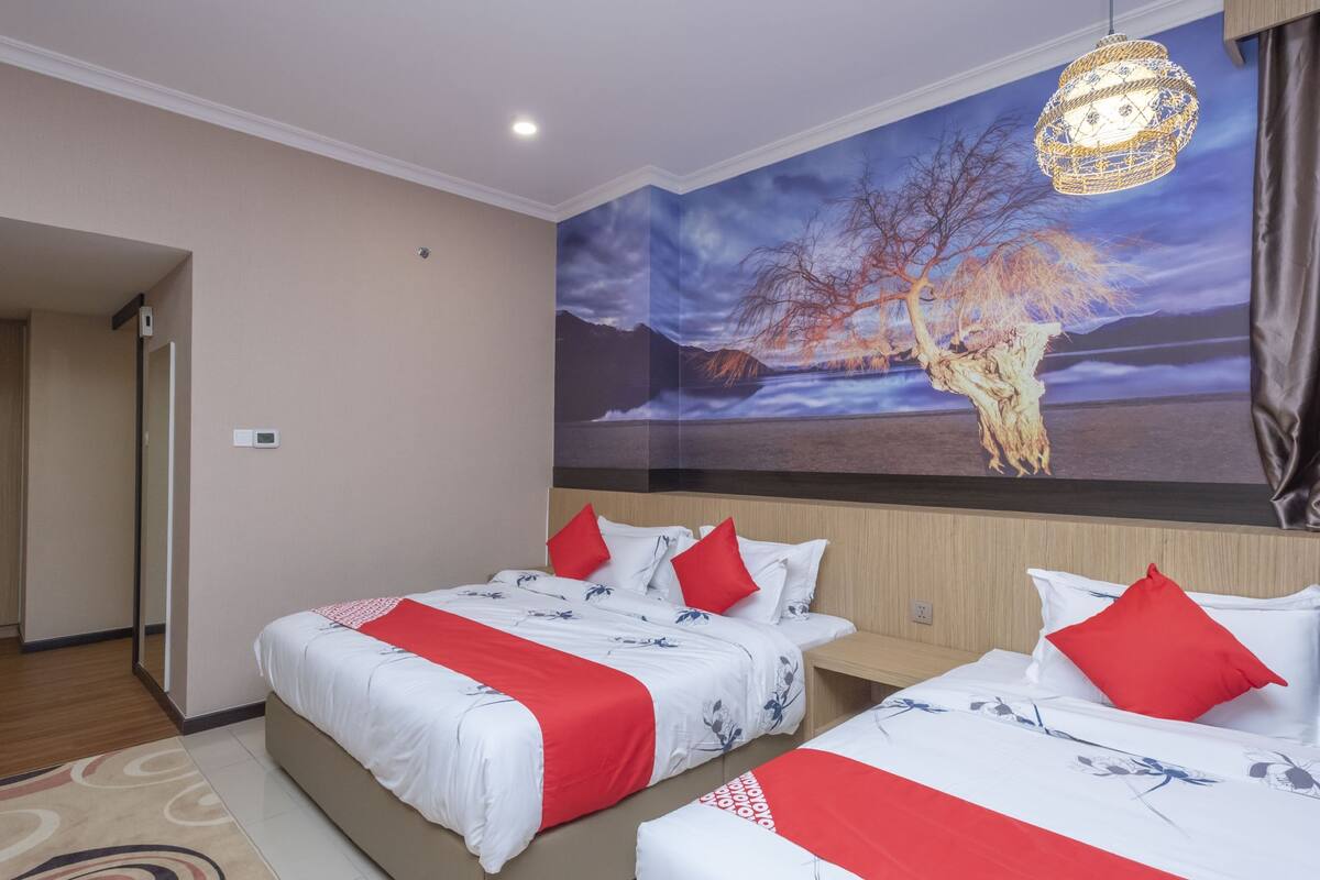 A hotel room with two beds, a large mural of a tree and landscape, and a hanging light fixture.