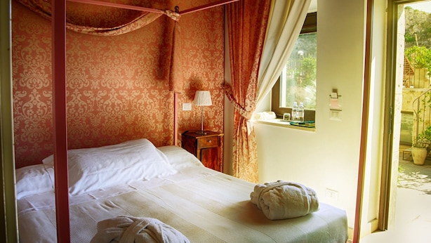 Ein Schlafzimmer mit Baldachinbett, Nachttisch mit Lampe und einem Fenster mit Blick auf Grünflächen.