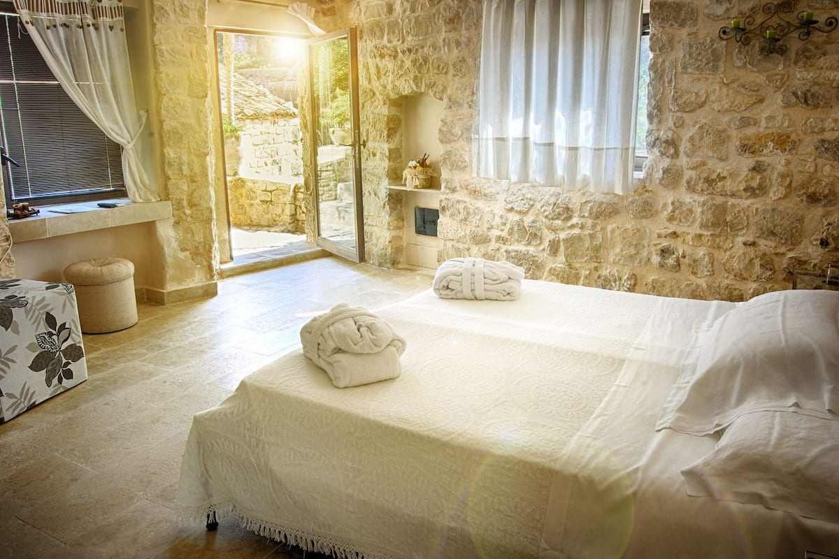 Une chambre confortable aux murs de pierre, dotée d’un grand lit et offrant une vue sur un escalier en pierre.