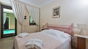 Ein Schlafzimmer mit einem Bett, einem Fenster mit Vorhängen, einem Nachttisch und einem Bild an der Wand.