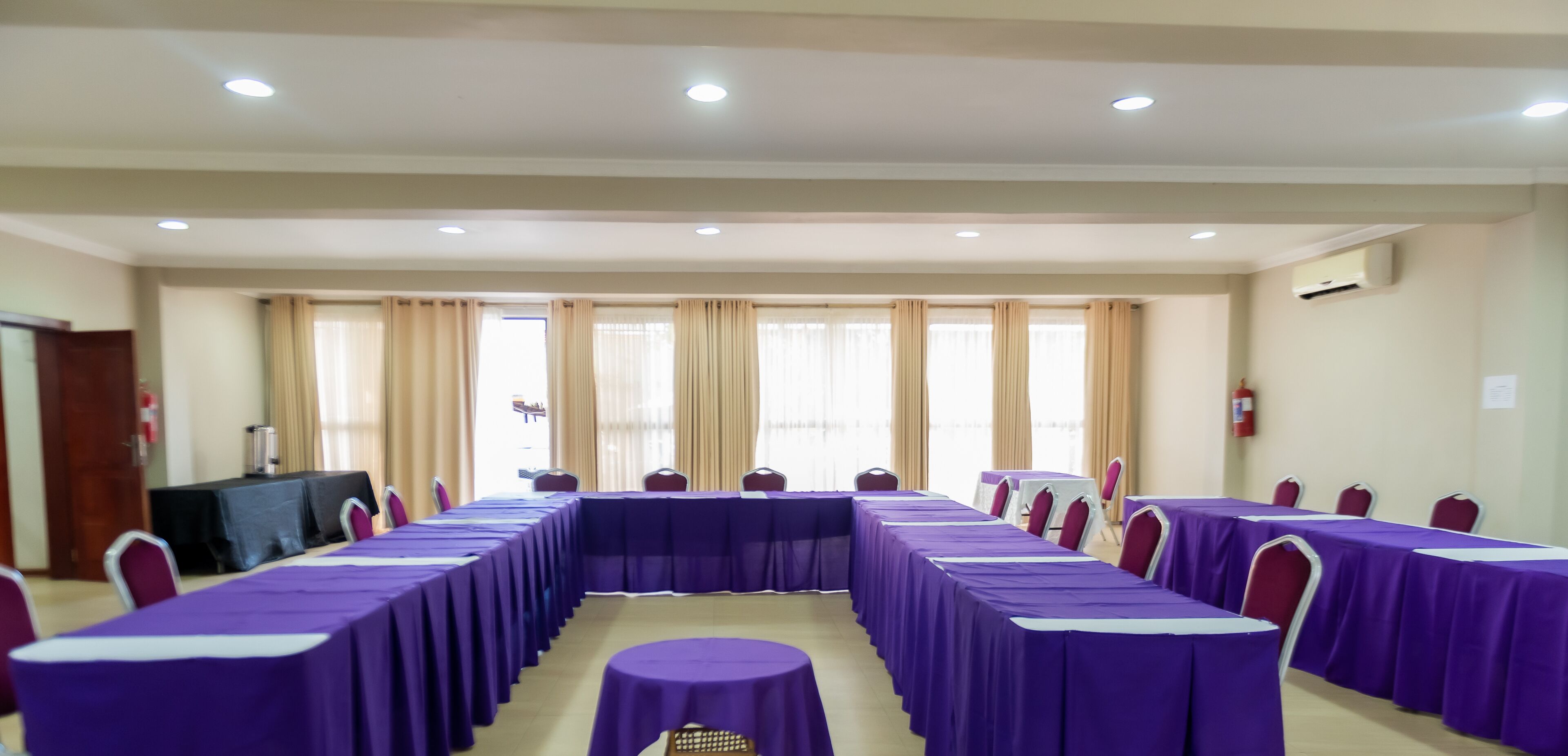 A conference room with long tables covered in purple tablecloths, arranged in a U-shape.