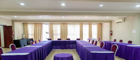 A conference room with long tables covered in purple tablecloths, arranged in a U-shape.