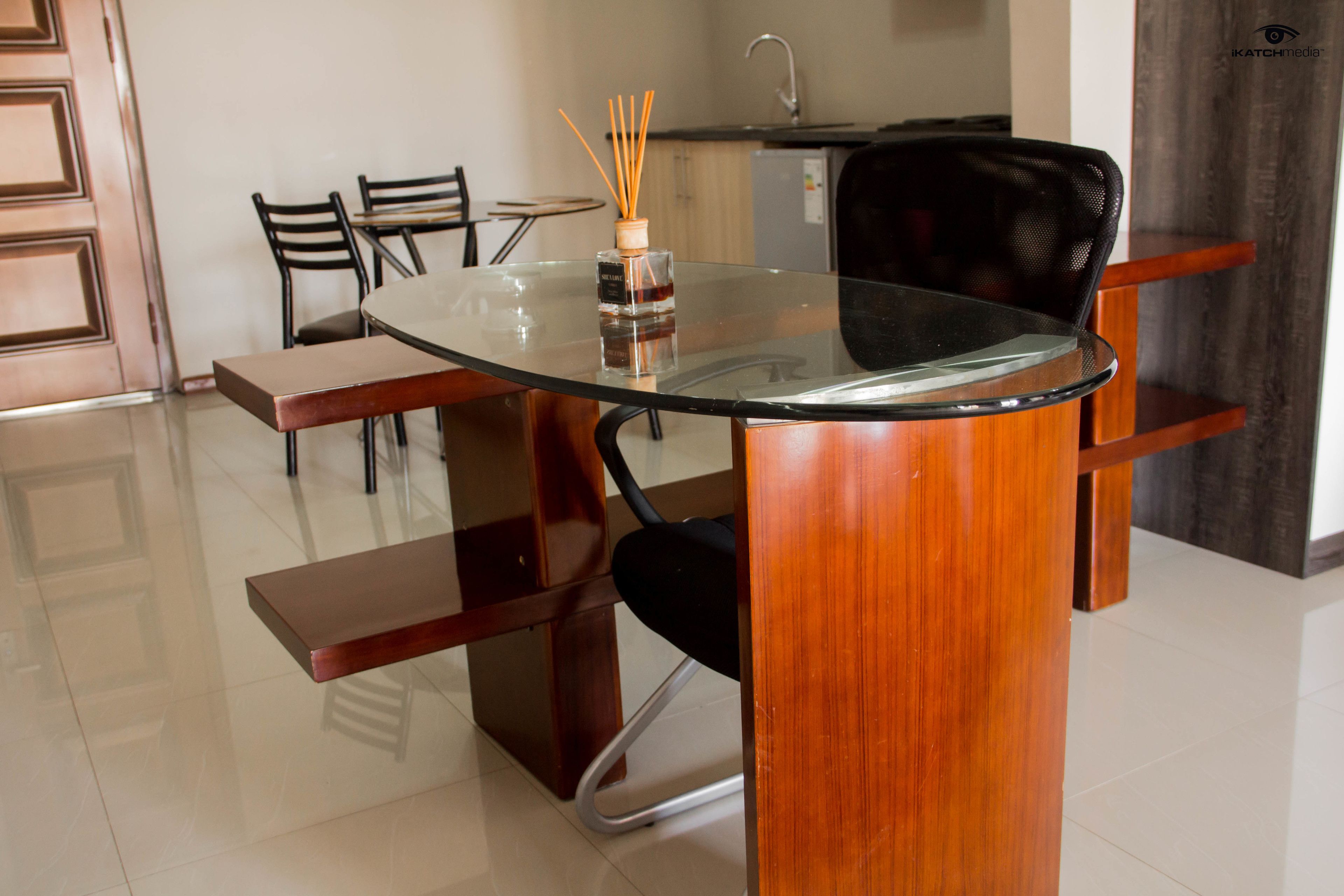 A dining area with a glass-top table, wooden chairs, and a small bottle of reed diffuser.