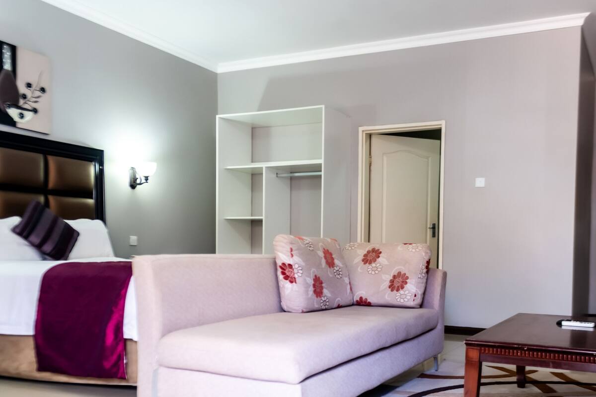 A modern hotel room with a bed, a sofa, a coffee table, and a wardrobe.