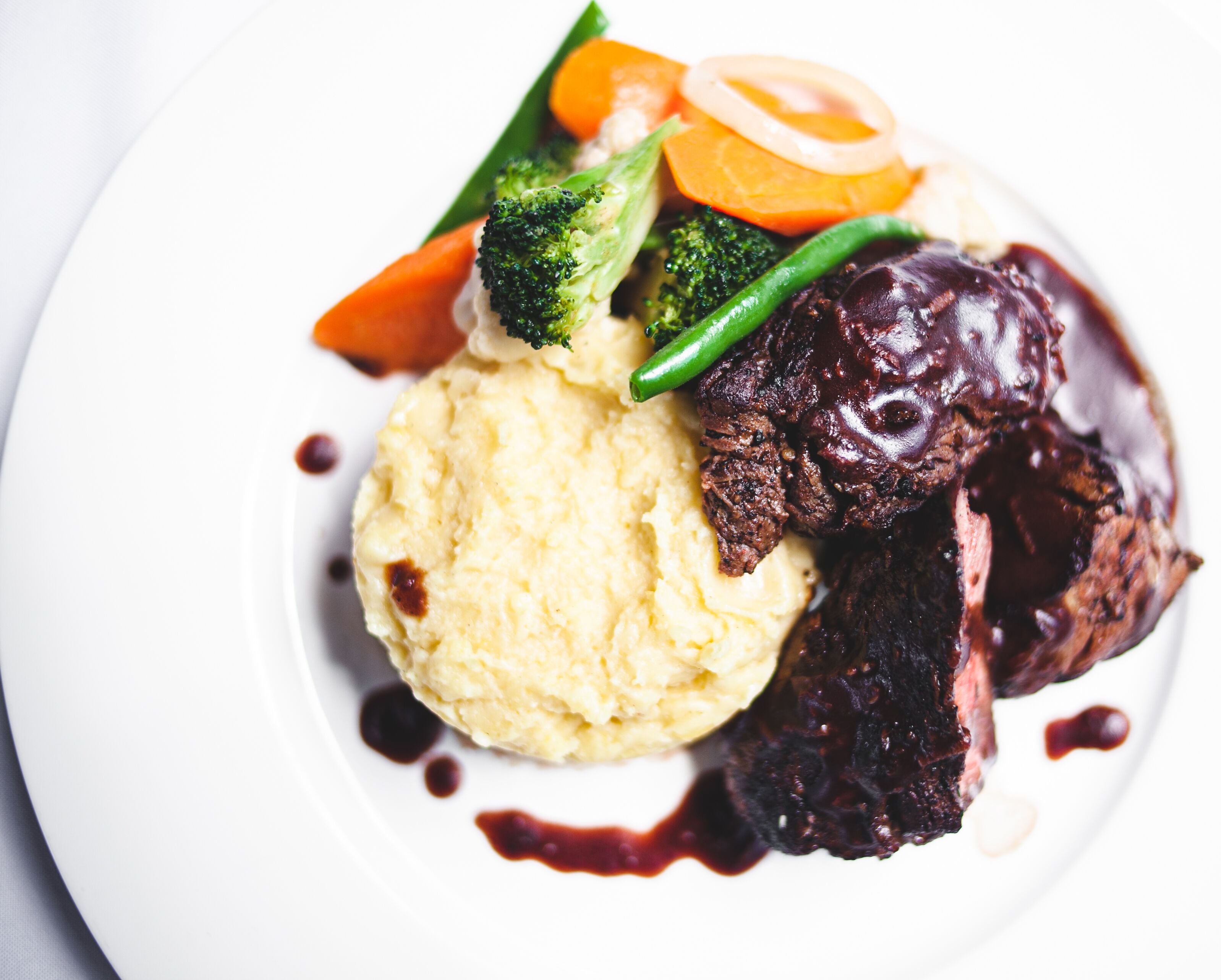 Une assiette contenant de la purée de pommes de terre, un morceau de viande et des légumes.
