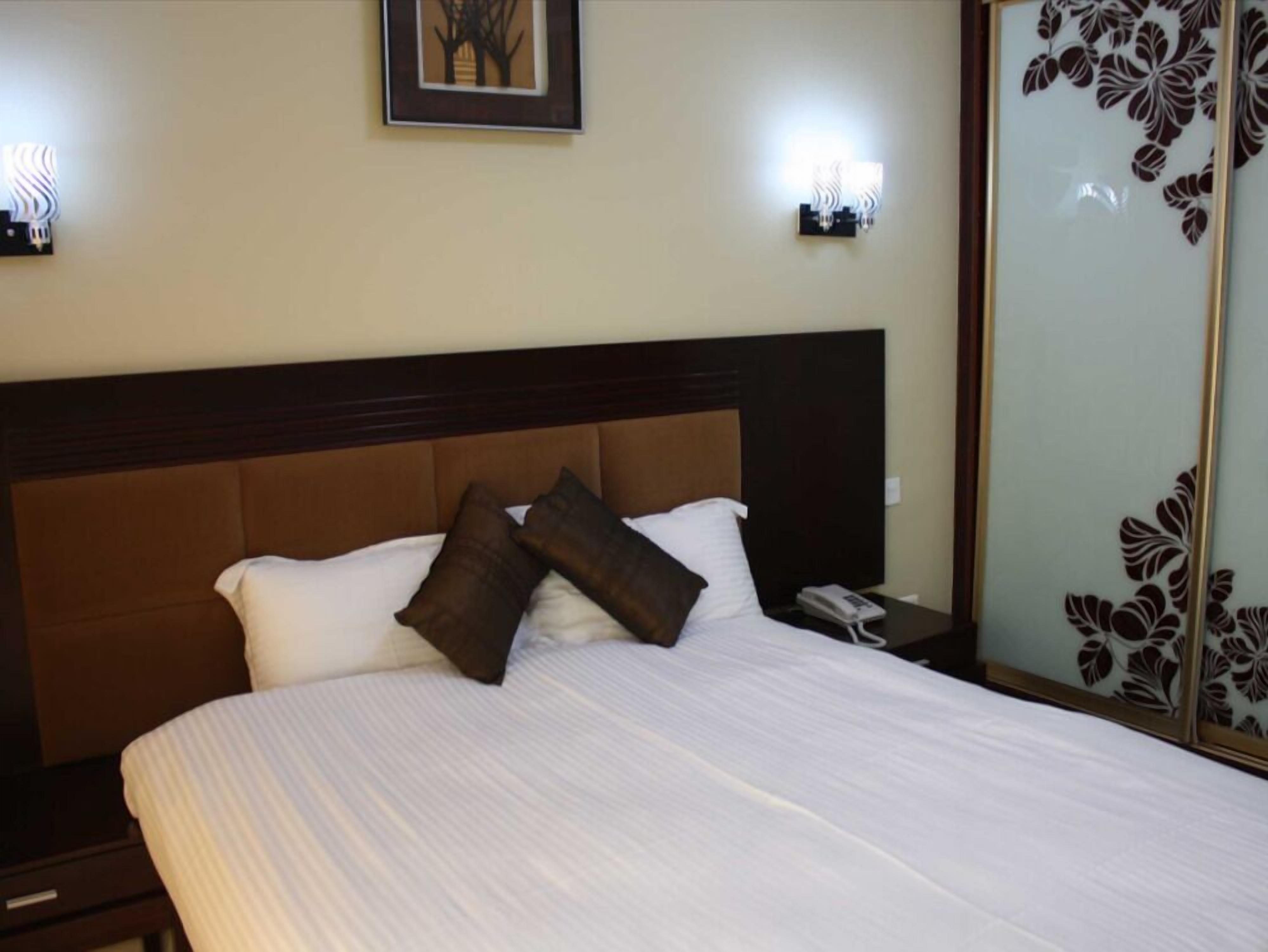 A hotel room with a large bed, two pillows, a bedside phone, and a nightstand.