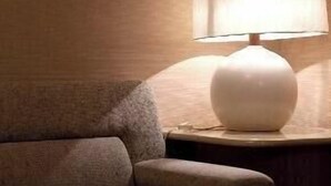 A modern room with a round table, a sofa, and a lamp on a wooden nightstand. - Maebashi Hotel (Maebashi)