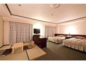 A hotel room with two beds, a desk, a chair, a television, and a window with curtains.