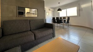 A modern living room with a grey sofa, a wooden coffee table, and a dining area with a table and chairs. - Drugstore B A - Two Bedroom Apartment, Sleeps 6 (Roses)