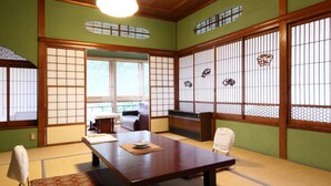 Ein traditioneller japanischer Raum mit Tatami-Boden, einem niedrigen Tisch, einer Couch und Schiebetüren.